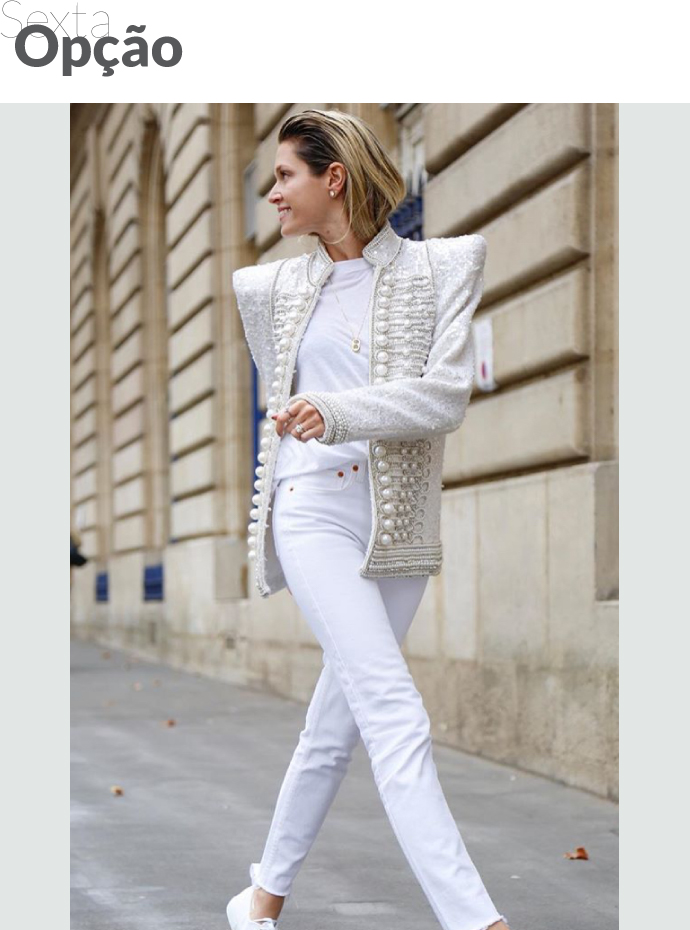 Uma mulher usa camisa e jeans branco, com uma jaqueta com aplicações.